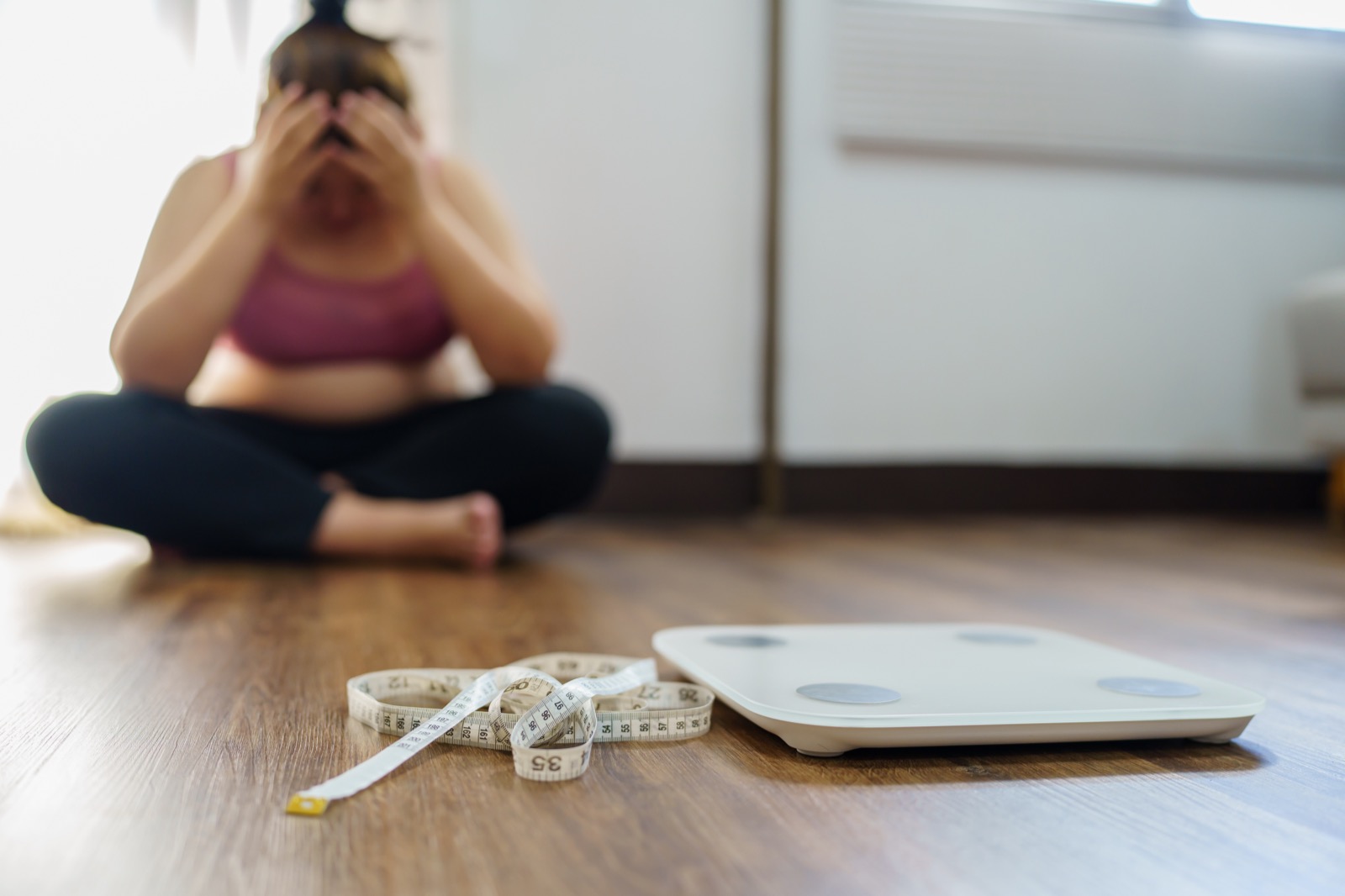 Woman sitting on the floor with her head in her hands, a scale and tape measure nearby
