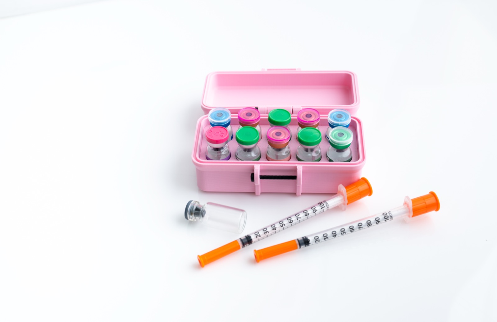 Pink carrying case containing colorful vials of gray-market peptides alongside orange syringes, arranged on a white surface